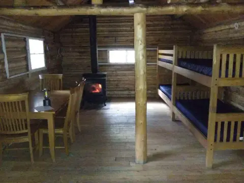 The interior of a rustic log cabin with bunk beds and a wood stove.
