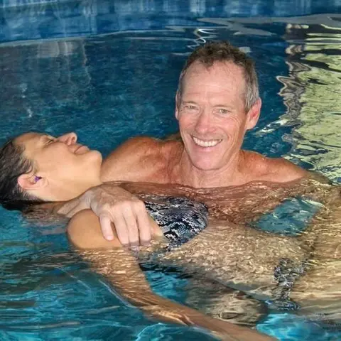 A man supports a woman floating in a swimming pool.