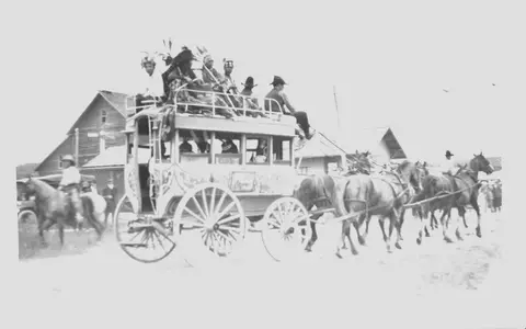 Historic black and white photograph of people riding on top of a horse-drawn omnibus.