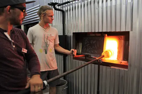 Two men working with hot glass at a furnace inside a studio.