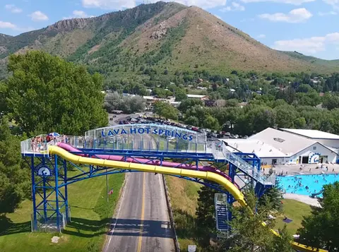 An aerial view of a water park with slides crossing over a road against a mountain backdrop.