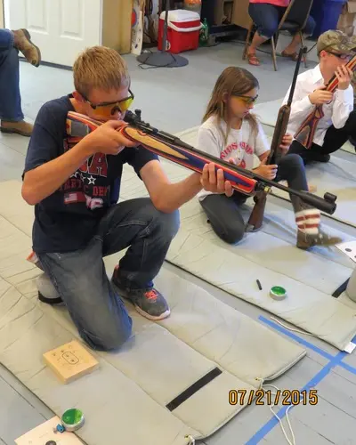 Children practice rifle shooting indoors on mats.
