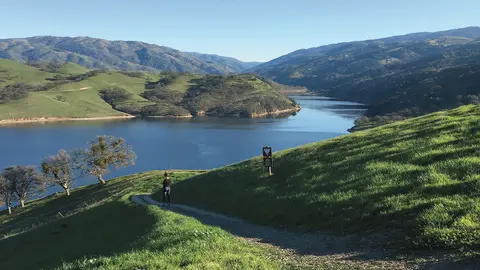 A person hiking on a trail overlooking a lake and hills.