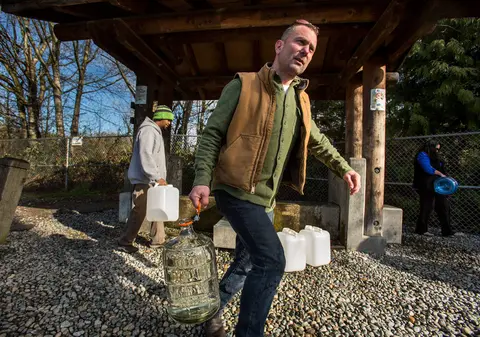 People carry large jugs of water from a filling station.