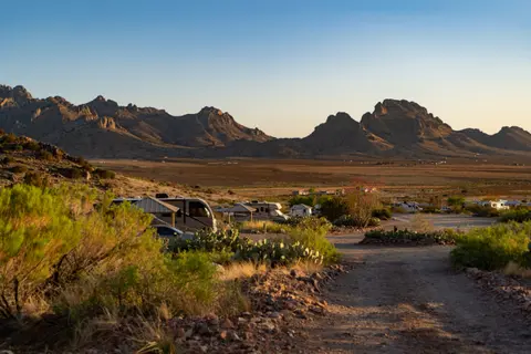 A desert landscape features mountains under a clear blue sky and a campground with RVs in the foreground.