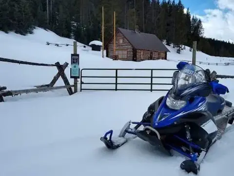 A snowmobile parked in front of a snowy cabin and a fenced area.