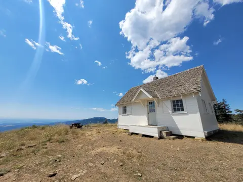 A white cabin stands on a grassy hilltop under a bright blue sky.