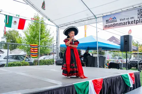 A young girl in traditional dress sings on an outdoor stage.