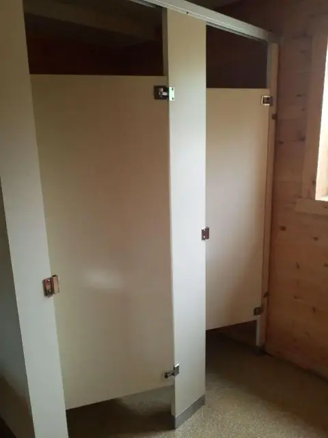 Interior view showing public restroom stalls with light-colored doors inside a wood-paneled room.