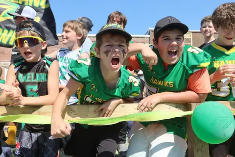 A group of young football players cheer excitedly behind a wooden barrier.