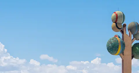 A colorful sculpture stands against a blue sky with clouds.