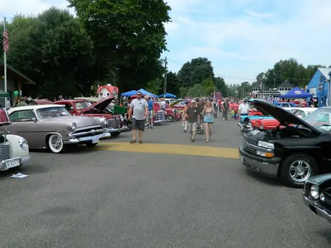A car show with people walking among vintage cars parked in an outdoor area.