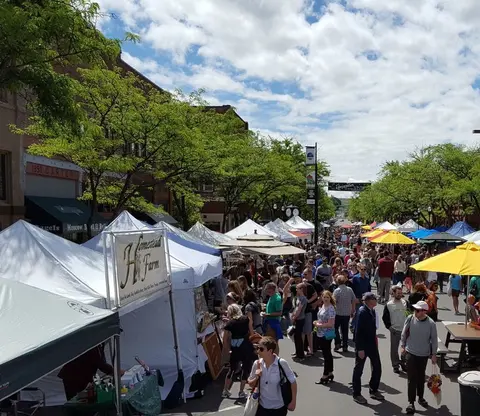 A crowded street fair with vendor tents and shoppers under a partly cloudy sky.