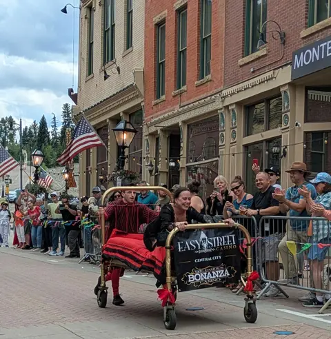People race a decorated bed down a street lined with spectators.