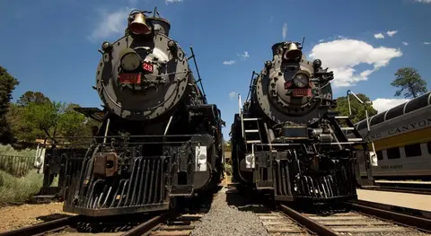 Two vintage steam locomotives parked on tracks outdoors under a blue sky.