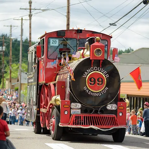 A red novelty train vehicle drives down a street during an outdoor event.