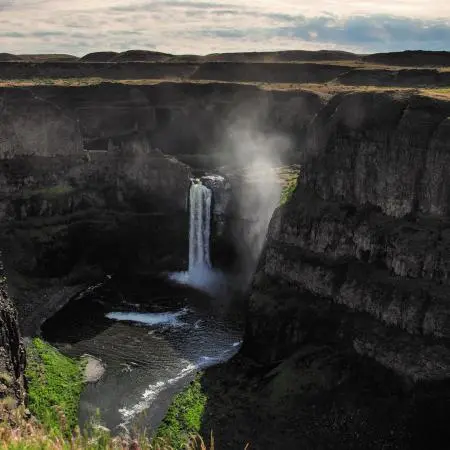 A tall waterfall flowing into a deep canyon with rocky cliffs.
