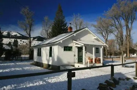 A small white house covered in snow with mountains in the background.