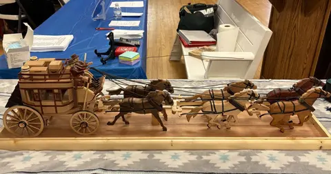 A detailed wooden model of a stagecoach with six horses rests on a table indoors.