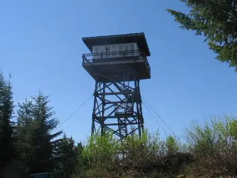 A wooden fire lookout tower stands among trees under a clear blue sky.