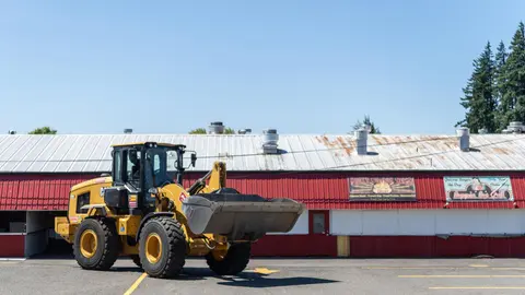 A yellow front loader is parked in a paved lot in front of a commercial building.