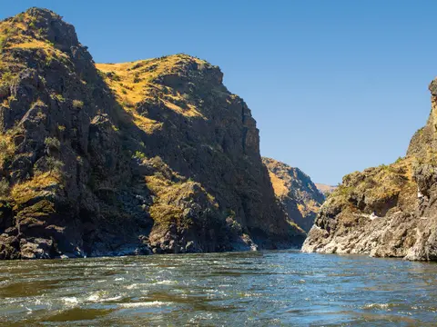 A wide river flows between steep, rocky canyon walls under a clear blue sky.
