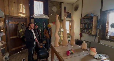 People stand in a pottery studio filled with ceramic art and shelves.