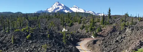 A winding road through a volcanic landscape with snow-capped mountains in the background.