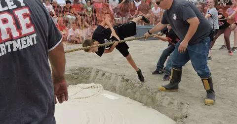 People participate in a tug-of-war game near a pit.