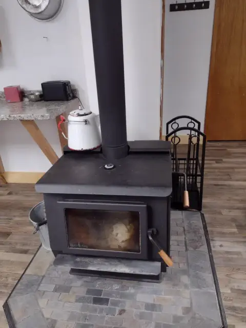 A wood-burning stove sits on a stone hearth inside a room.