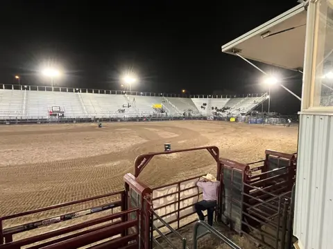 A person leaning on a fence overlooking a rodeo arena at night.
