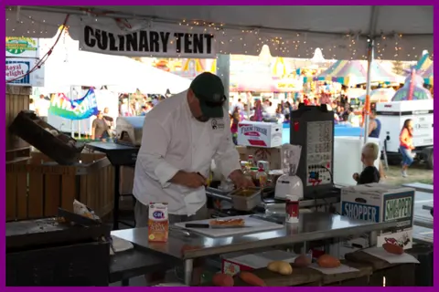 A chef prepares food in a culinary tent at an outdoor event.