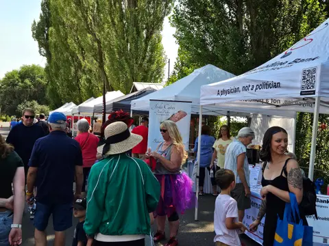 People stroll past white vendor tents at an outdoor market event.