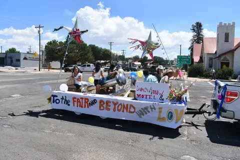 A parade float decorated with stars and a banner travels down a street.