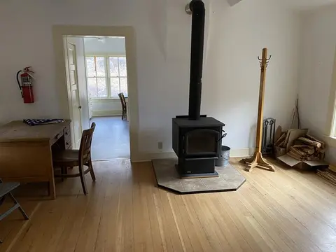 An interior room with a wood-burning stove, wooden floors, and a desk.
