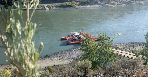 A ferryboat on a wide river with a ramp on the shore.
