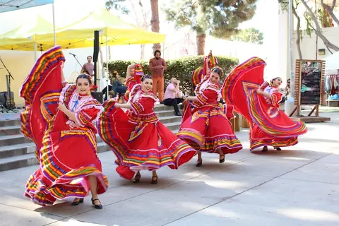 Four dancers in traditional red dresses perform outdoors.