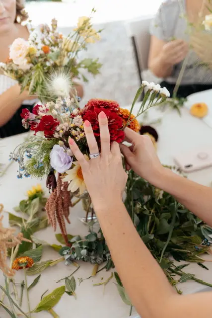 A person arranges colorful flowers on a table during a workshop.