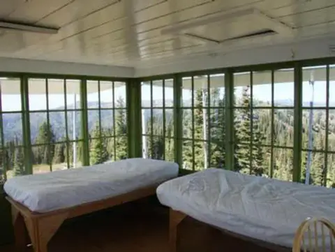 Two beds inside a room with large windows overlooking a forest.