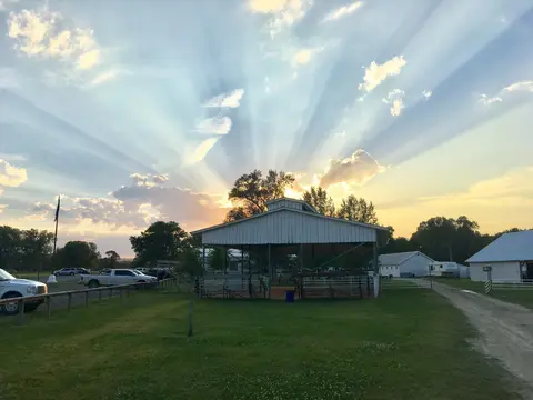 A sunset with dramatic sun rays radiating over an open pavilion and surrounding farm buildings.