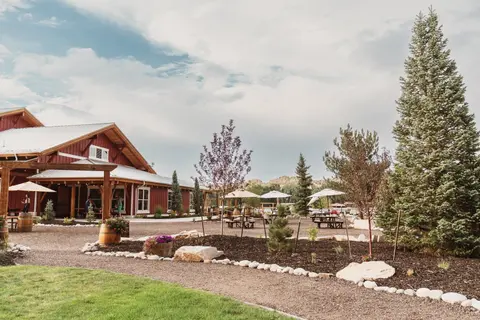 A red barn-like building stands next to a gravel path with picnic tables and trees.