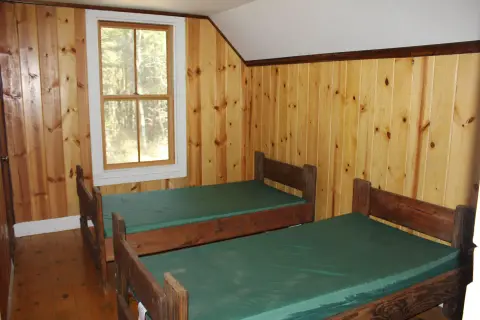 An interior view of a bedroom with wooden paneled walls and two twin beds.