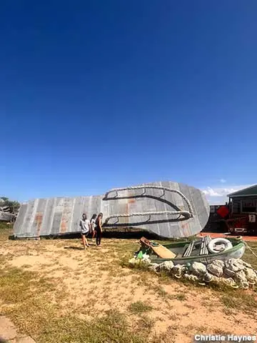 A giant flip-flop sculpture resting on the ground with people standing nearby.