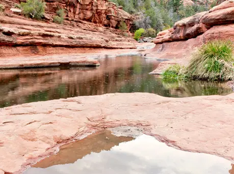 A narrow stream flows between red rock formations.