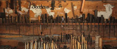 A collection of old tools hangs on a wooden wall.