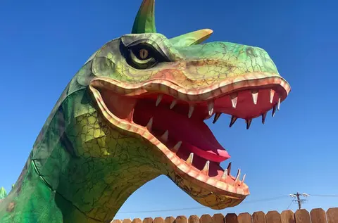 A close-up view of a large green dinosaur sculpture with an open mouth against a blue sky.