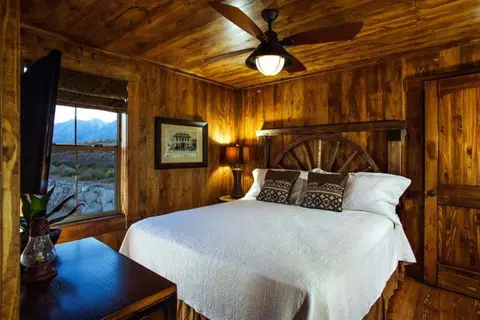A rustic wooden bedroom with a large bed, ceiling fan, and window showing mountains.