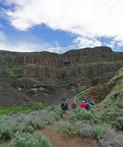 A group of people hiking on a trail toward rocky cliffs.
