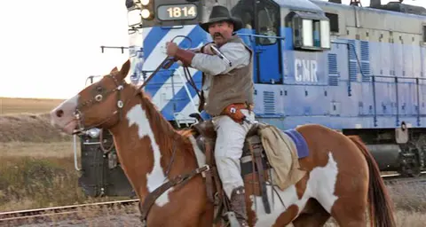 A man on horseback rides alongside a train.