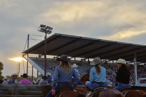 People on horseback watch an event from an arena.